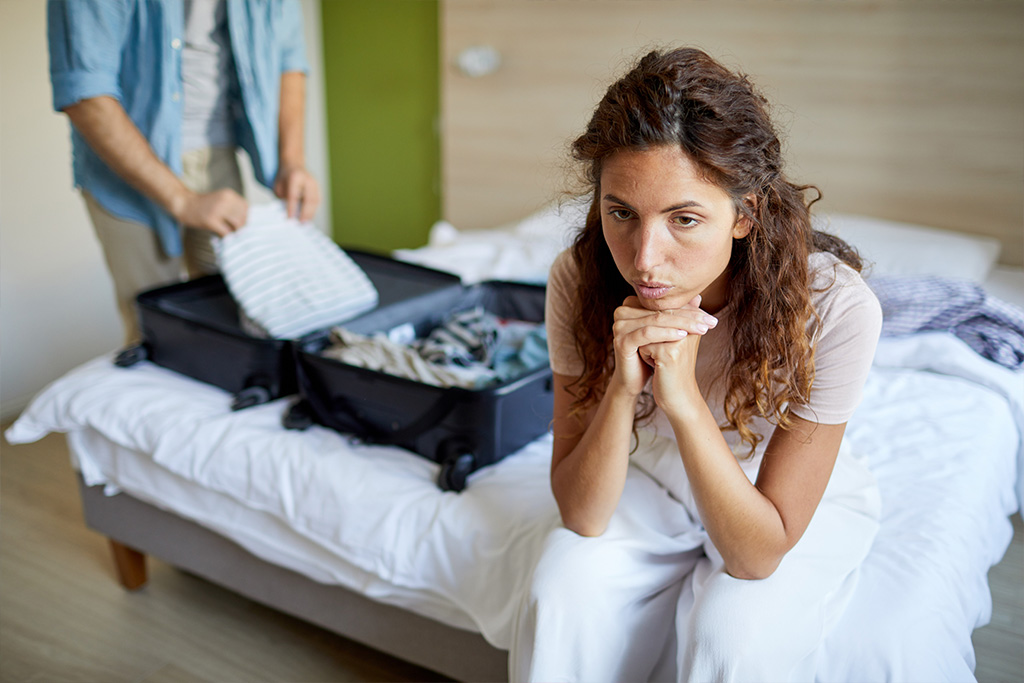 Jak poradzić sobie z rozstaniem? - kobieta siedzi na łóżku, jej partner pakuje walizkę - artykuł Marity Woźny