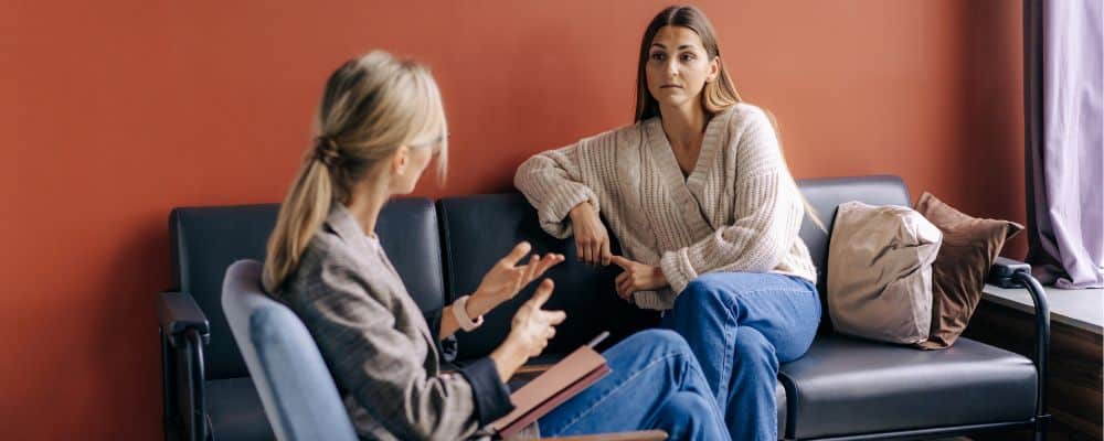 Jak wygląda pierwsza wizyta u psychoterapeuty - kobieta siedząca na kanapie u psychoterapeuty pyta, czy do psychologa potrzebne jest skierowanie - blog Marita Woźny