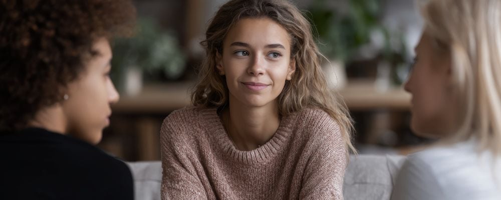 Dlaczego ciągle trafiam na niewłaściwe osoby w relacjach koleżeńskich i przyjaźniach? - kobieta siedząca na wprost dw&oacute;ch koleżanek milczy, bo nie chce konfliktu - psychoterapia Marita Woźny