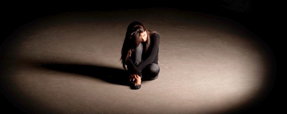 Lęk przed odrzuceniem &ndash; jak sobie z nim radzić - smutna kobieta siedząca na podłodze pośrodku ciemnego pomieszczenia obrazująca uczucie lęku - psychoterapia Wrocław 